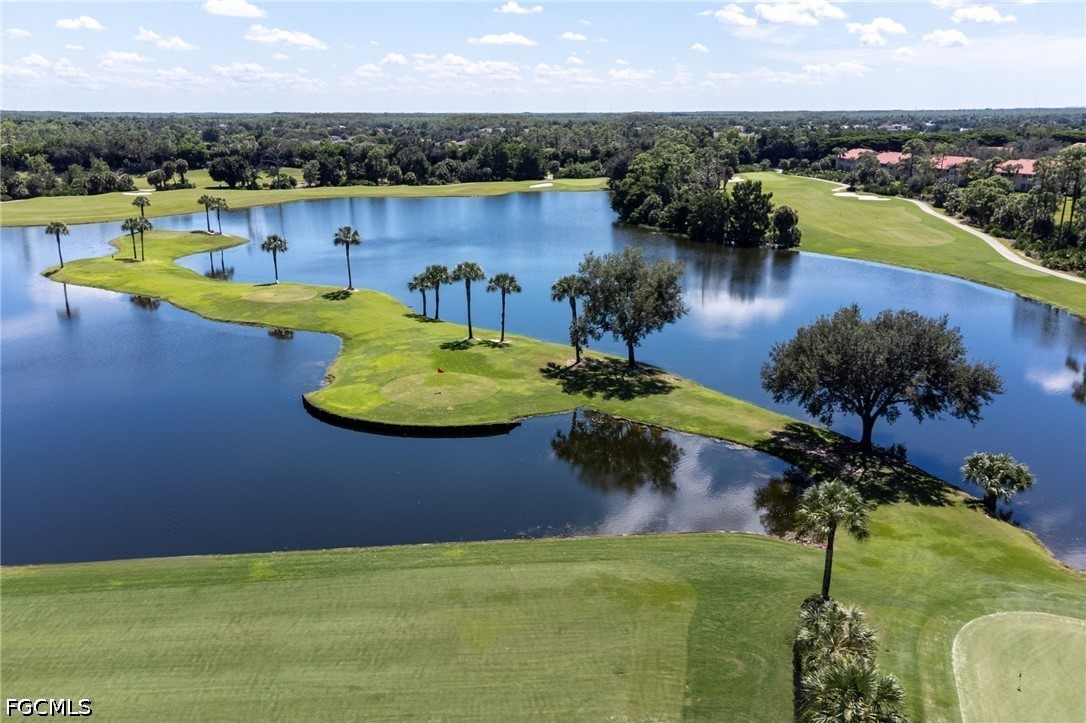 Aerial golf course with a lake winding around grassy greens and palm trees.