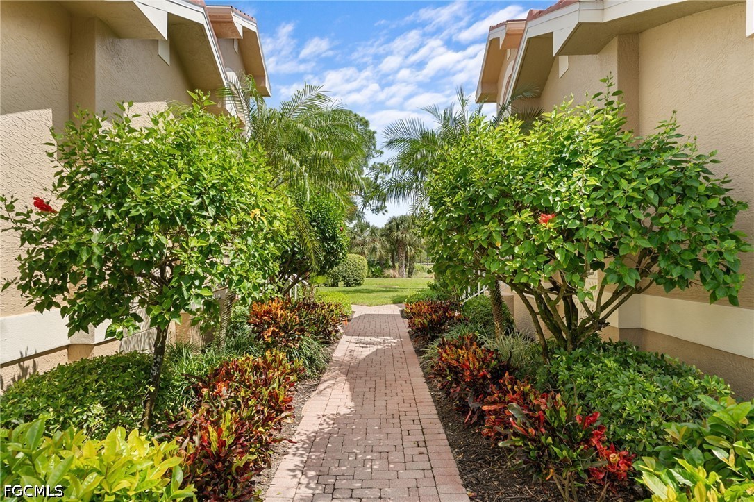 Brick walkway between beige residential buildings, lined with tropical palms and colorful landscaping.