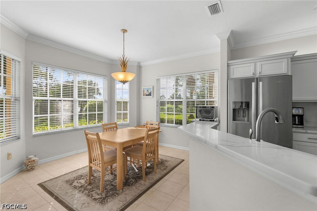 Kitchen and dining area with a wood table, white breakfast bar, and large windows overlooking greenery.