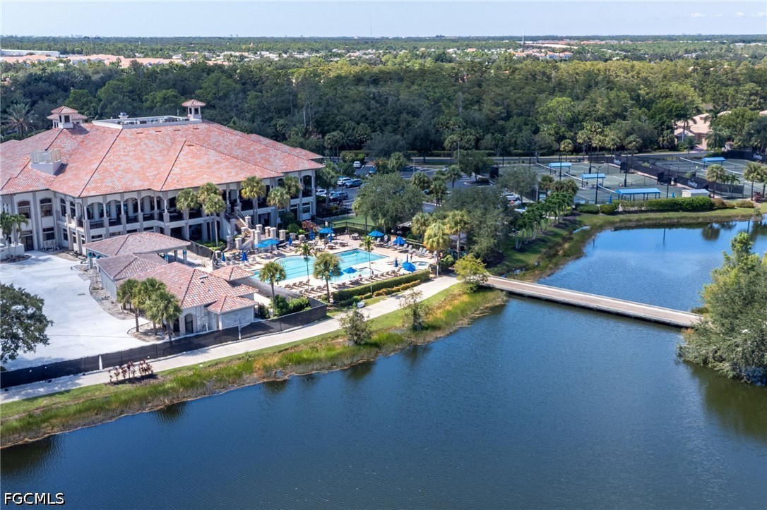 Community clubhouse, pool, and tennis courts beside a lake crossed by a bridge.