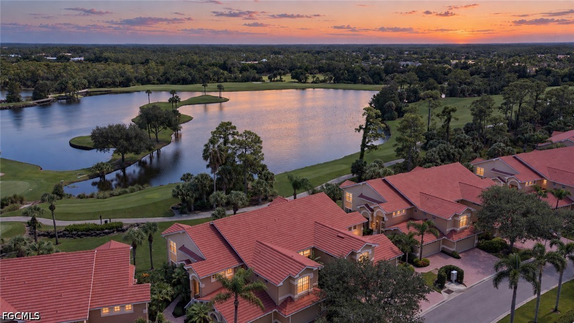 Aerial view of red-roofed homes beside a lake and golf course at sunset.