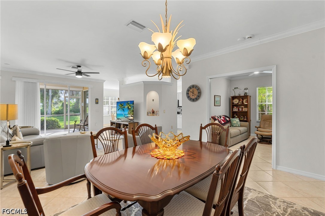 Dining room with a wooden table beneath a chandelier, opening to a furnished living area.