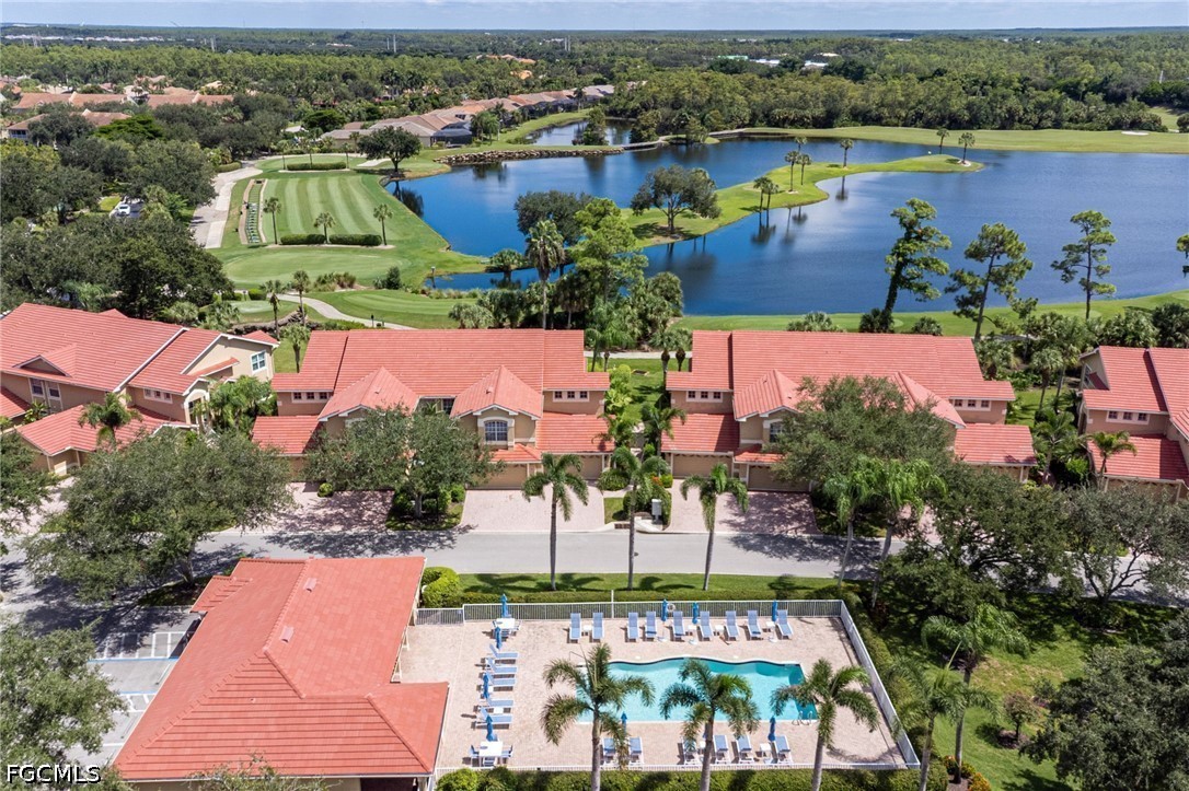 Aerial view of red-roofed homes, a community pool, and golf course beside a lake.