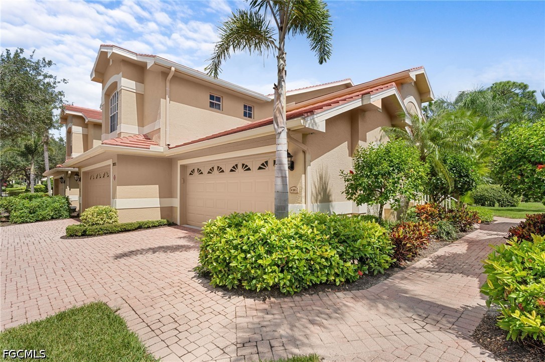 Two-story beige home with attached garages, red tile roofs, and tropical landscaping.