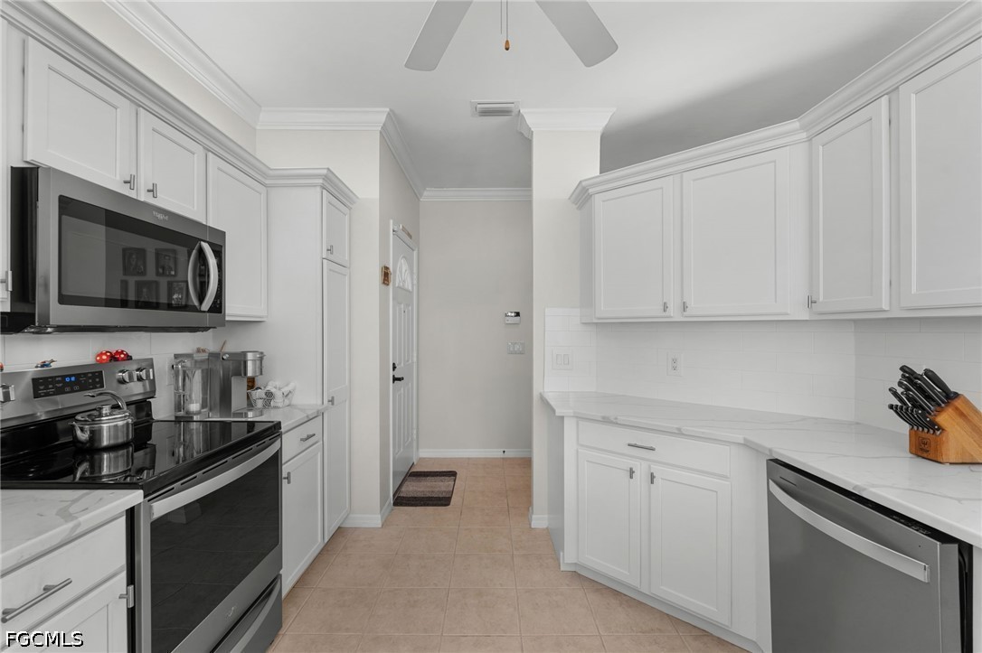 Kitchen with white shaker cabinets, stainless steel appliances, and tan tile flooring.