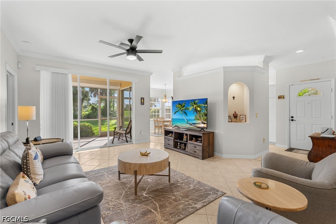 Furnished living room with gray sofas and sliding glass doors overlooking a green lawn and palm trees.