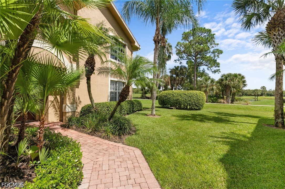Beige home beside a brick walkway, palm trees, and a manicured golf course lawn.