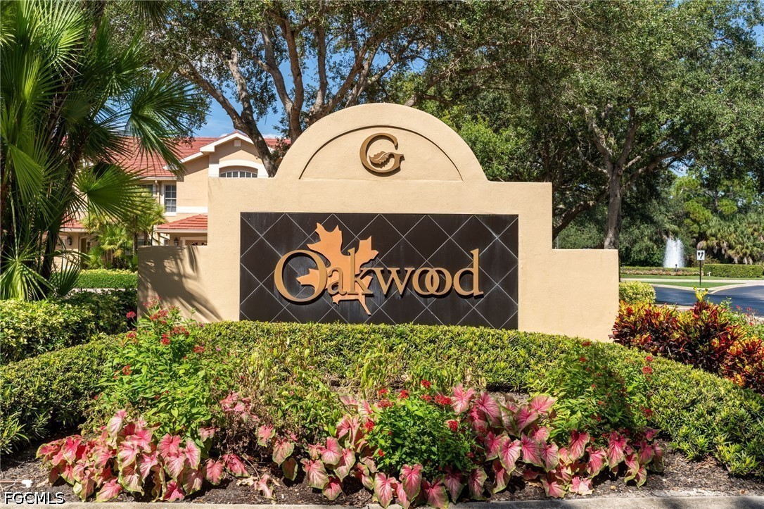 Oakwood community entrance sign amid flowering plants, with a fountain in the background.