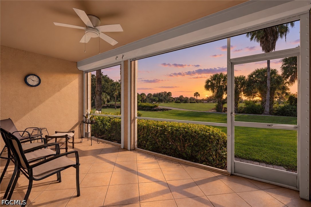 Screened lanai with tiled floor and seating overlooking a palm-lined golf course at sunset.