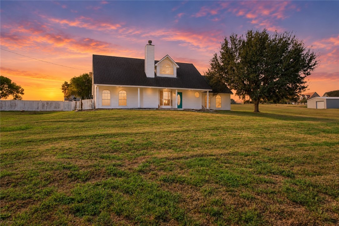 White farmhouse with a dark roof and green front door at sunset.