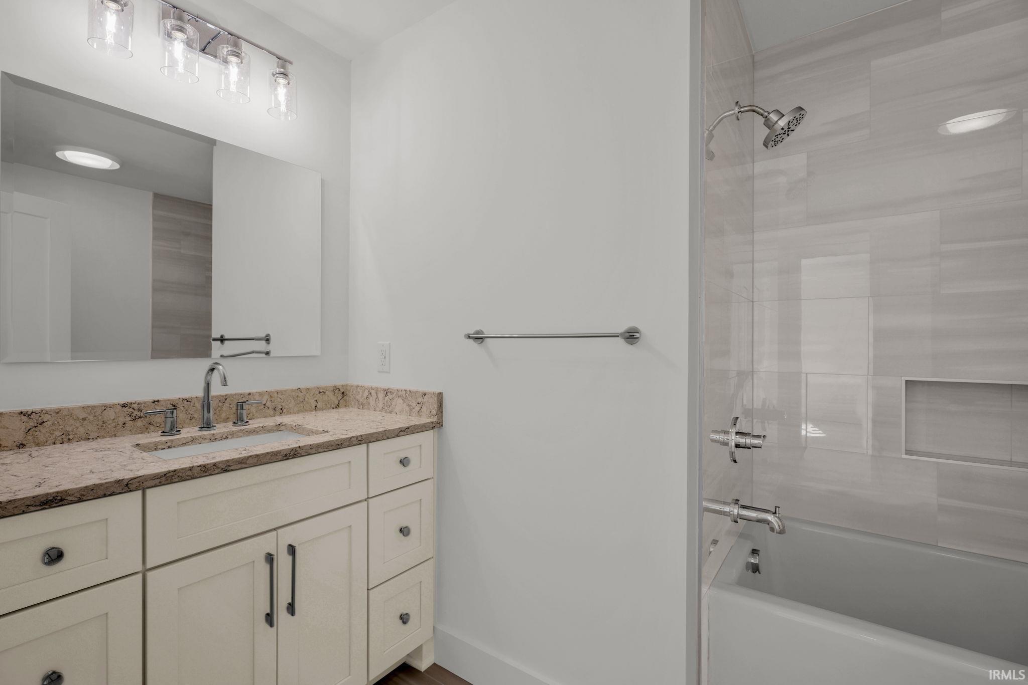 Bathroom with a cream vanity and stone countertop beside a tiled tub-shower.