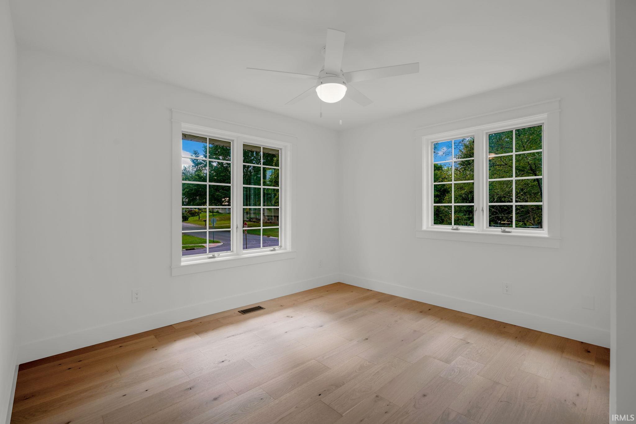 Unfurnished room with light wood floors, a ceiling fan, and two sets of windows.