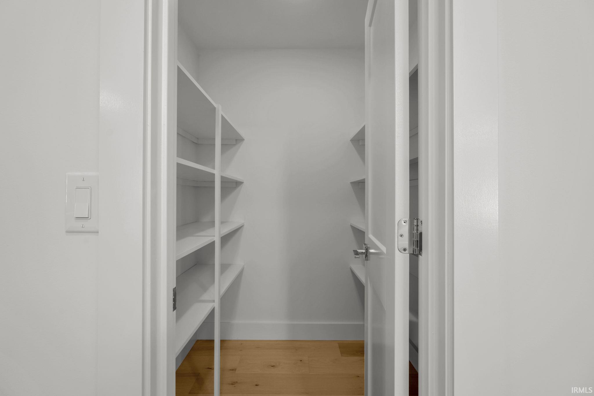 Walk-in closet with white built-in shelves along both sides and light wood flooring.