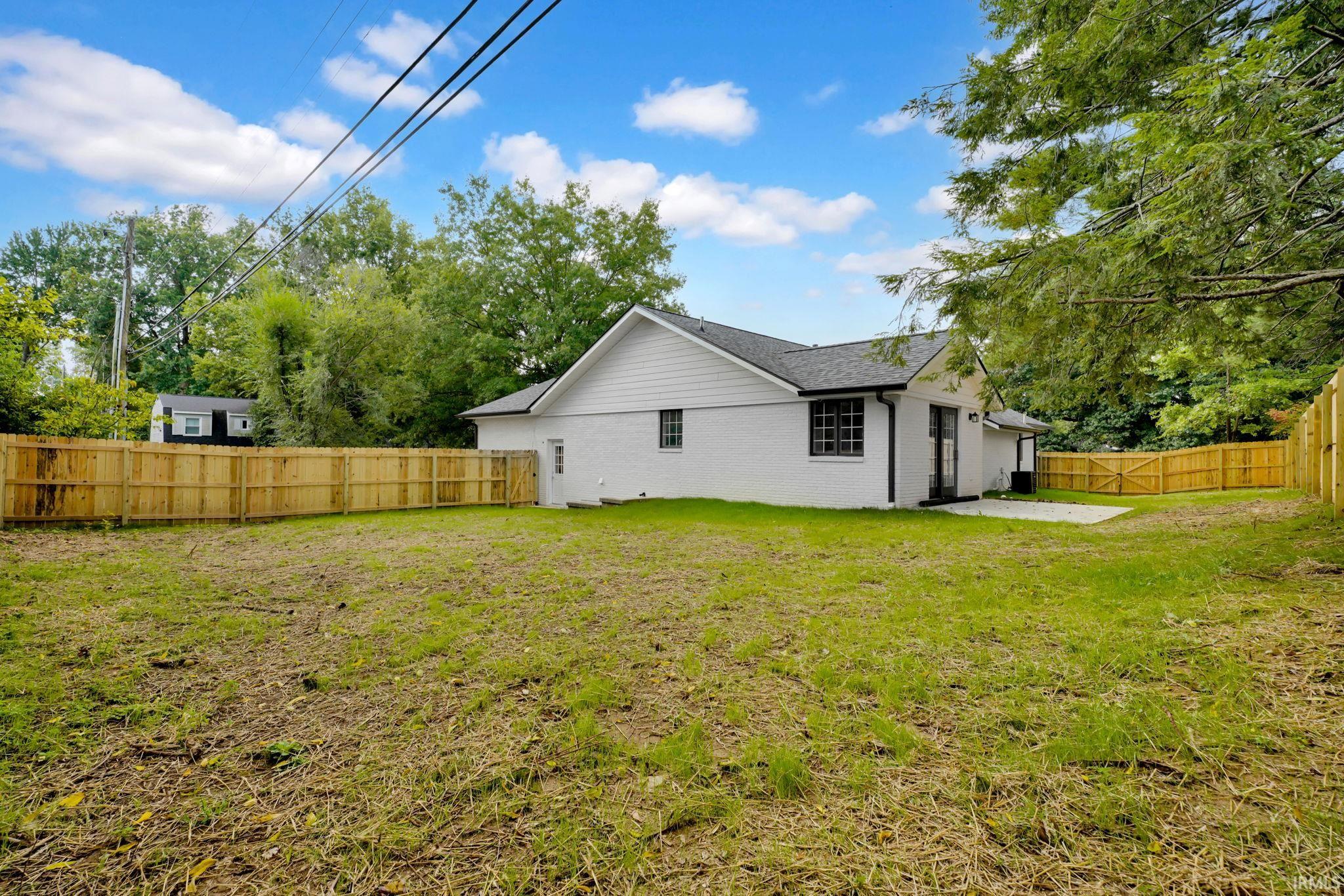 White brick home with a fenced backyard and concrete patio.