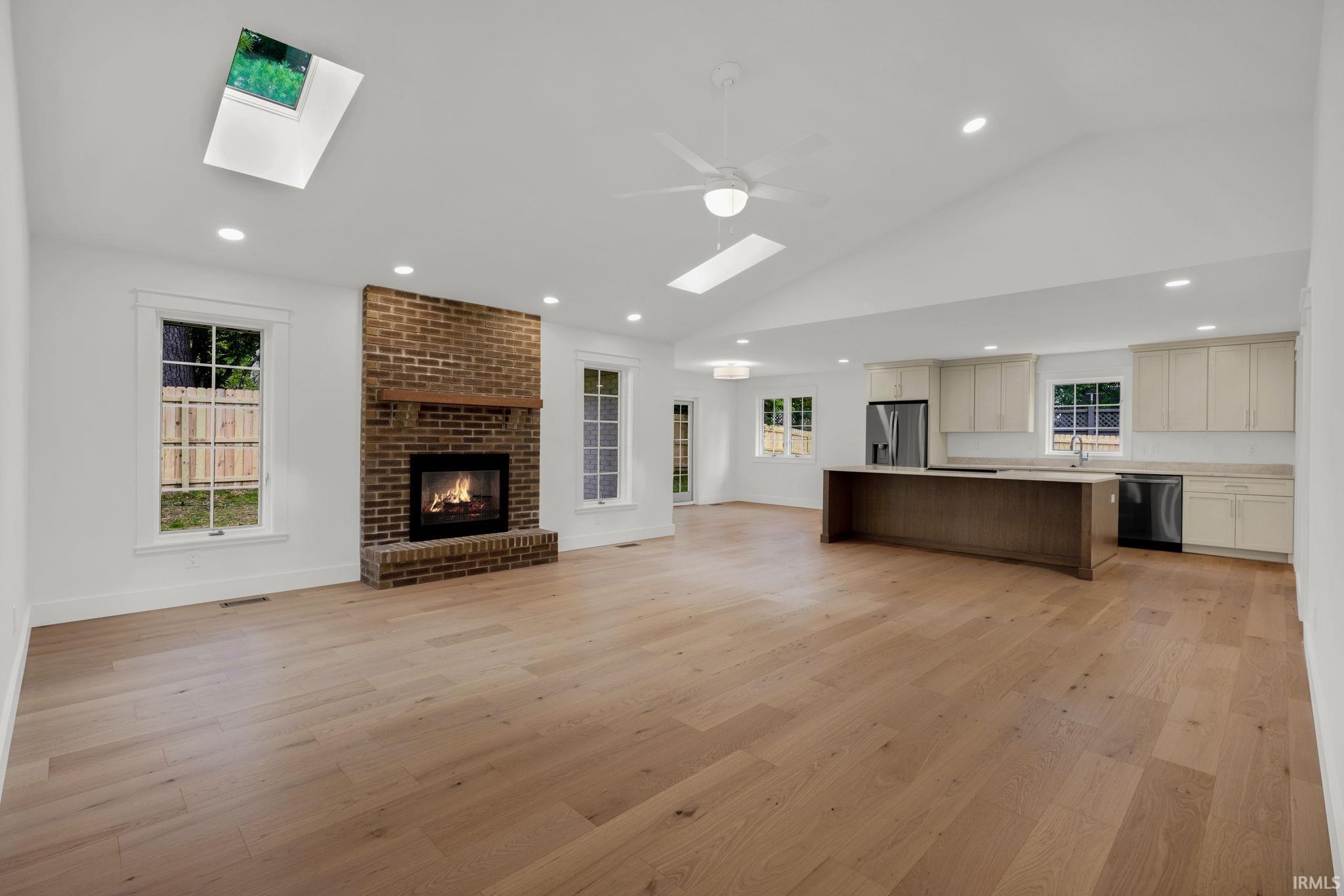 Open-plan living room and kitchen with a brick fireplace, skylights, and a large dark island.