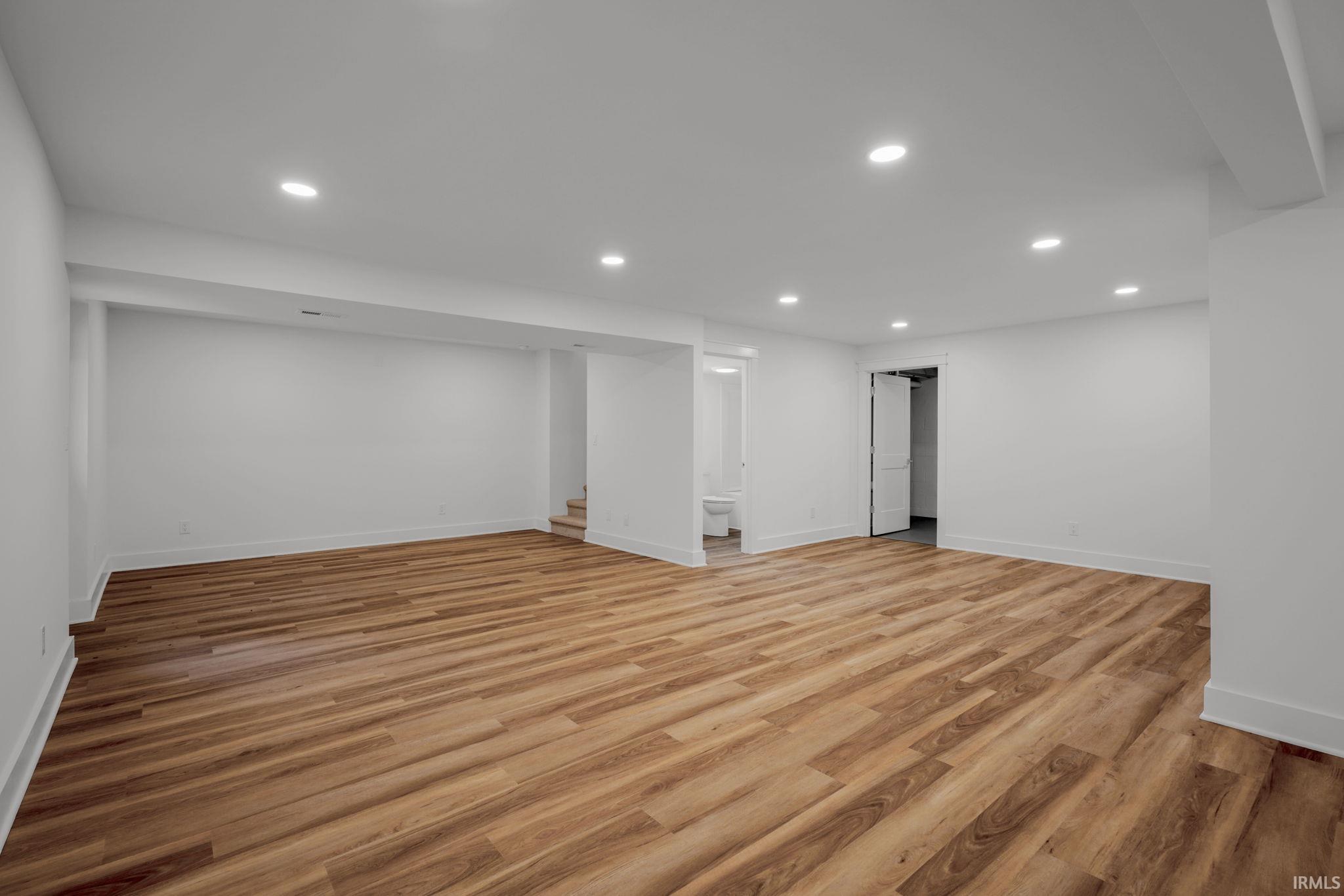 Vacant interior room with warm wood-look flooring, recessed lights, and a doorway to a bathroom.