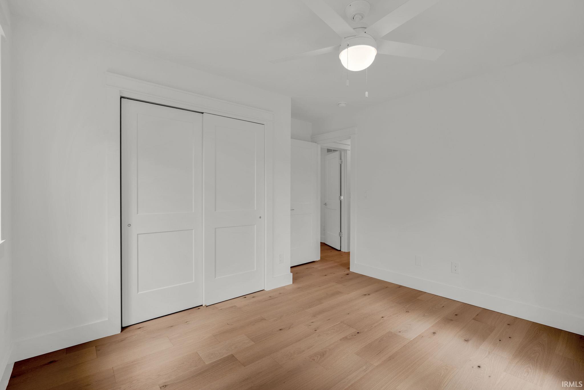 Empty bedroom with light hardwood floors, paneled closet doors, and a ceiling fan.