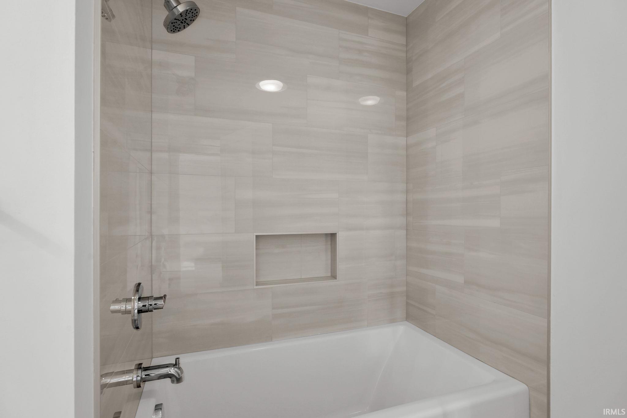 Tiled bathtub and shower with a recessed niche and chrome fixtures.