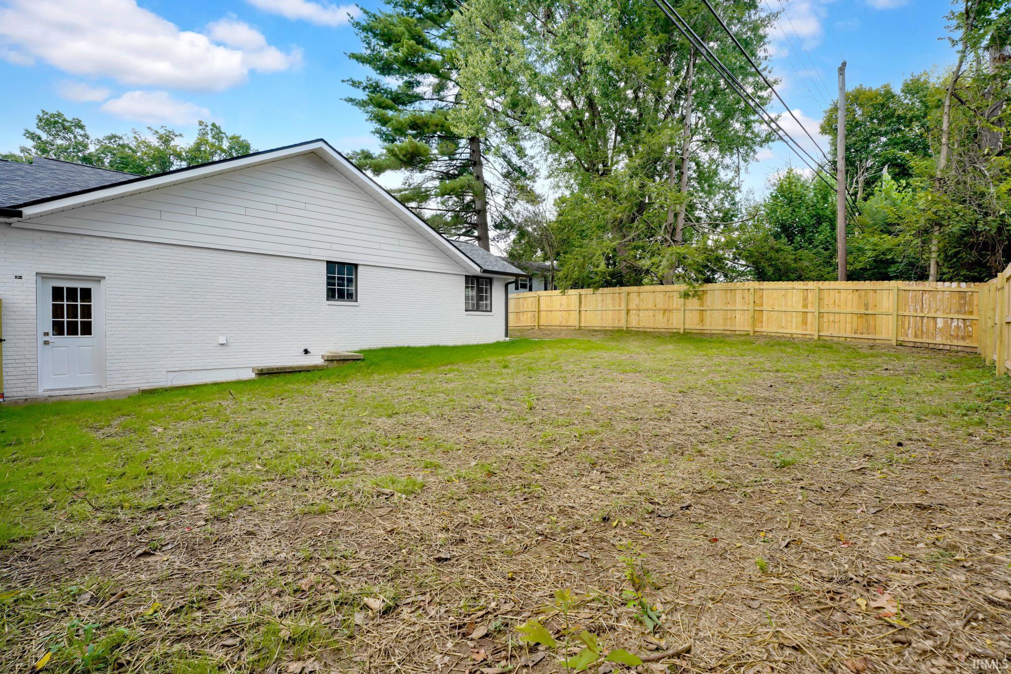 Backyard with a mostly bare lawn, wooden privacy fence, and white brick house.