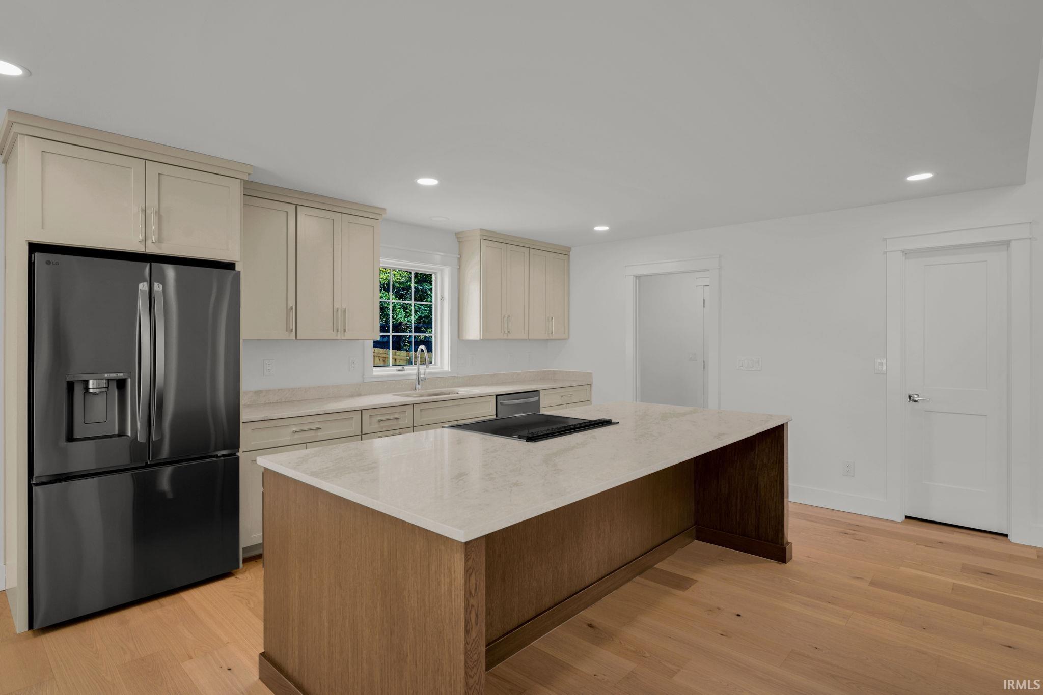 Kitchen with a large wood-paneled island, pale stone countertop, black cooktop, and dark refrigerator.