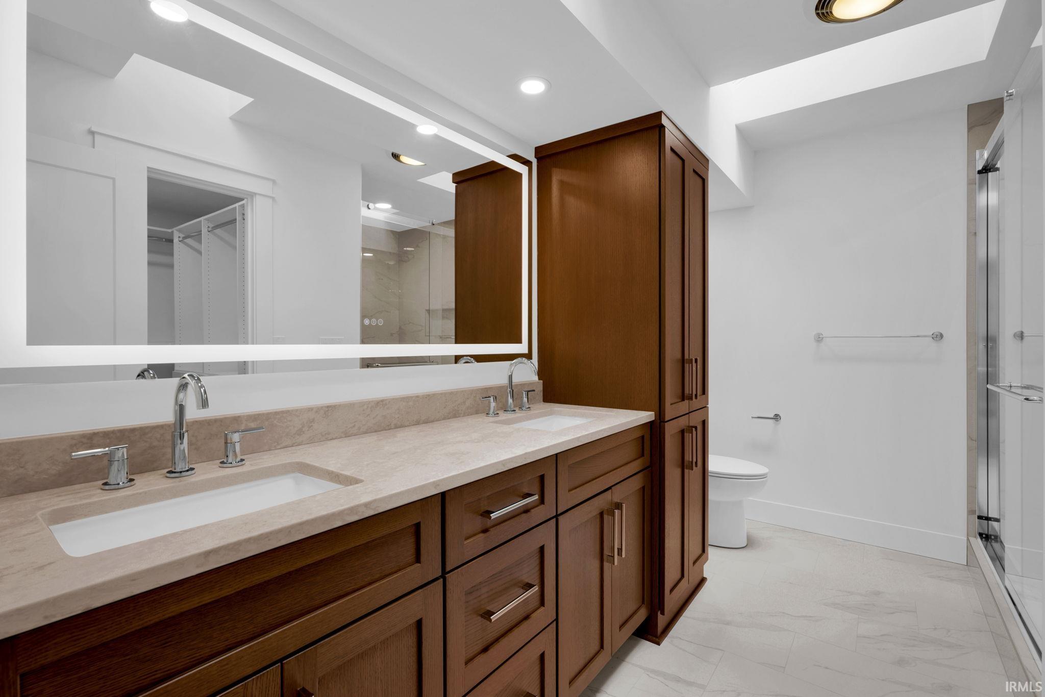 Bathroom with a long double-sink vanity, dark wood cabinetry, and glass-enclosed shower.