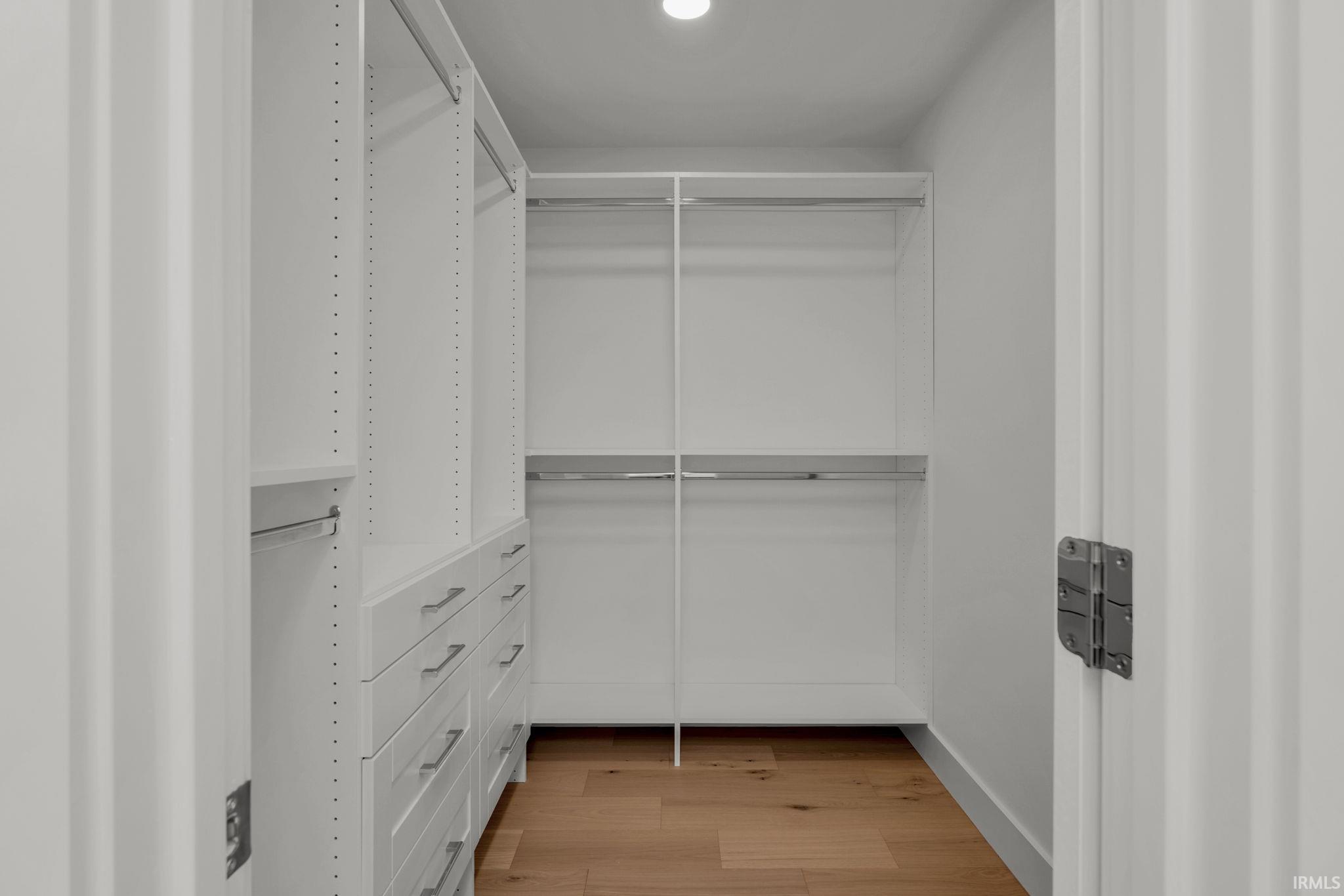 Walk-in closet with white built-in drawers and shelving, double hanging rods, and a wood floor.