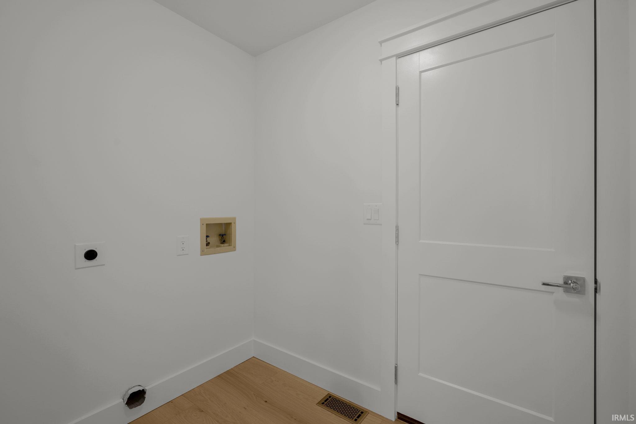 Empty laundry area with washer hookups, a white paneled door, and light wood flooring.