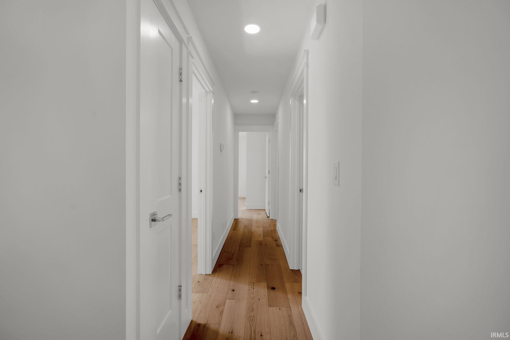 White hallway with warm hardwood floors, recessed lights, and doors along both sides.