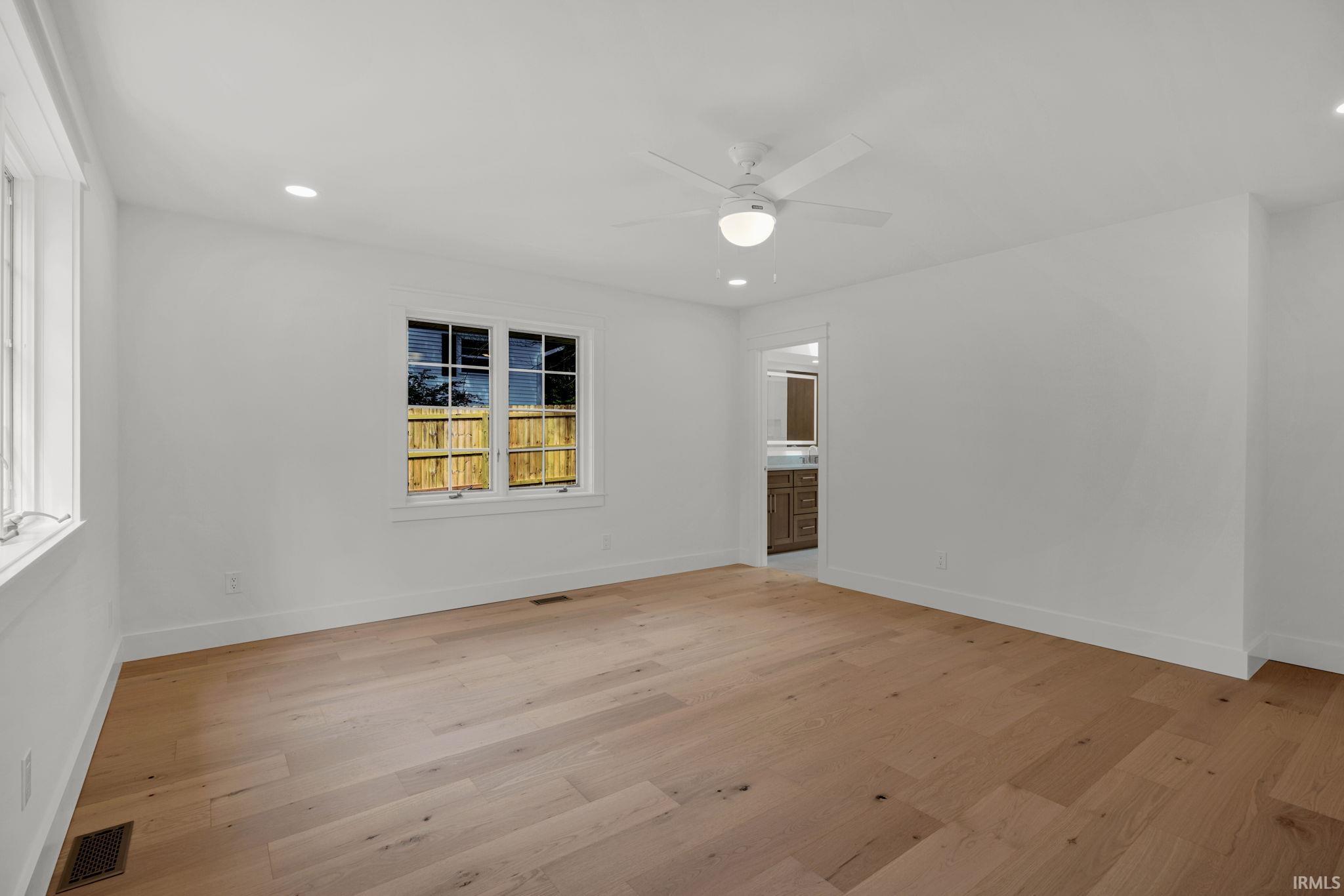 Empty room with wide-plank hardwood floors, a ceiling fan, and a doorway to a bathroom.