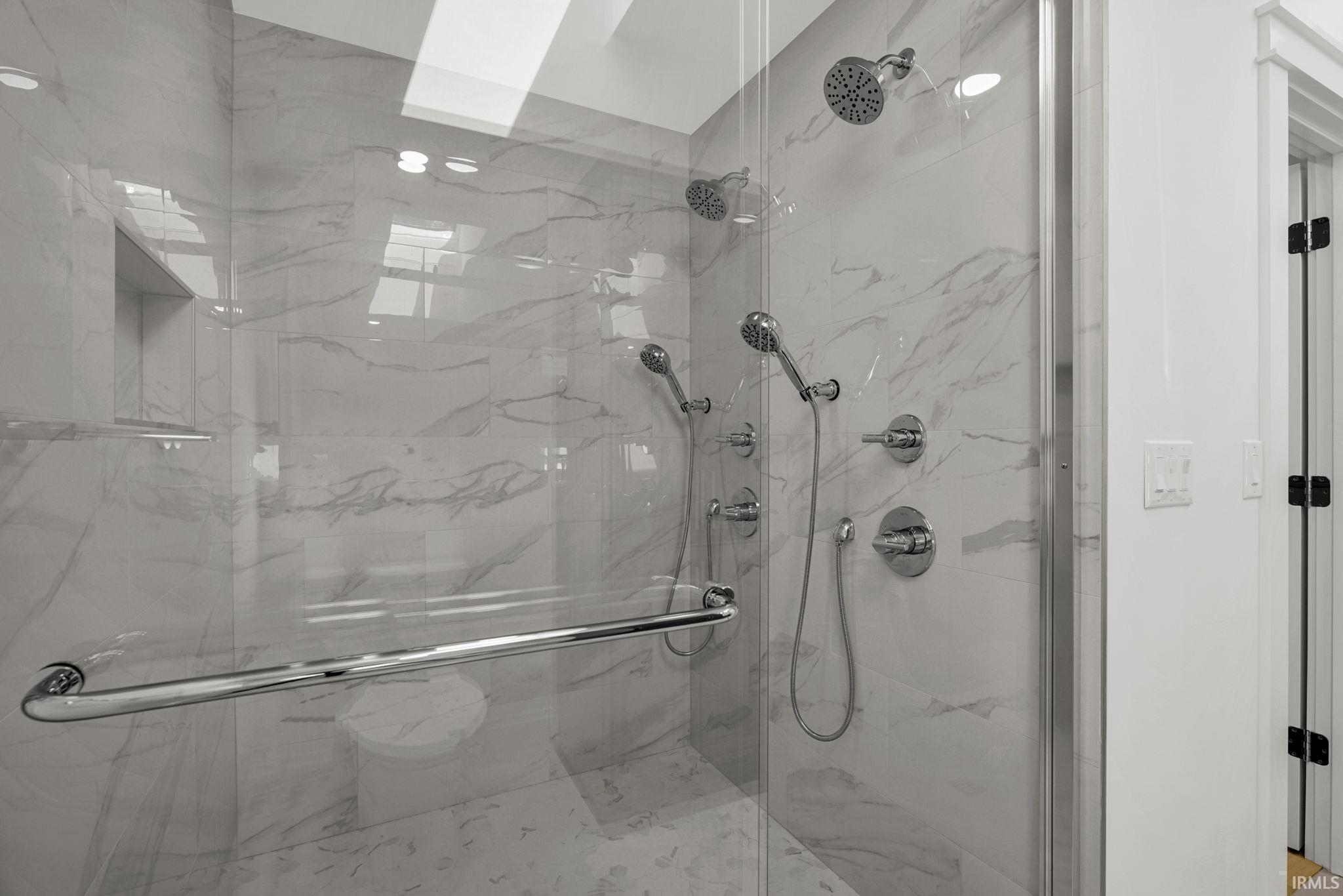 Walk-in shower with marble-look tile, glass enclosure, and multiple chrome showerheads.