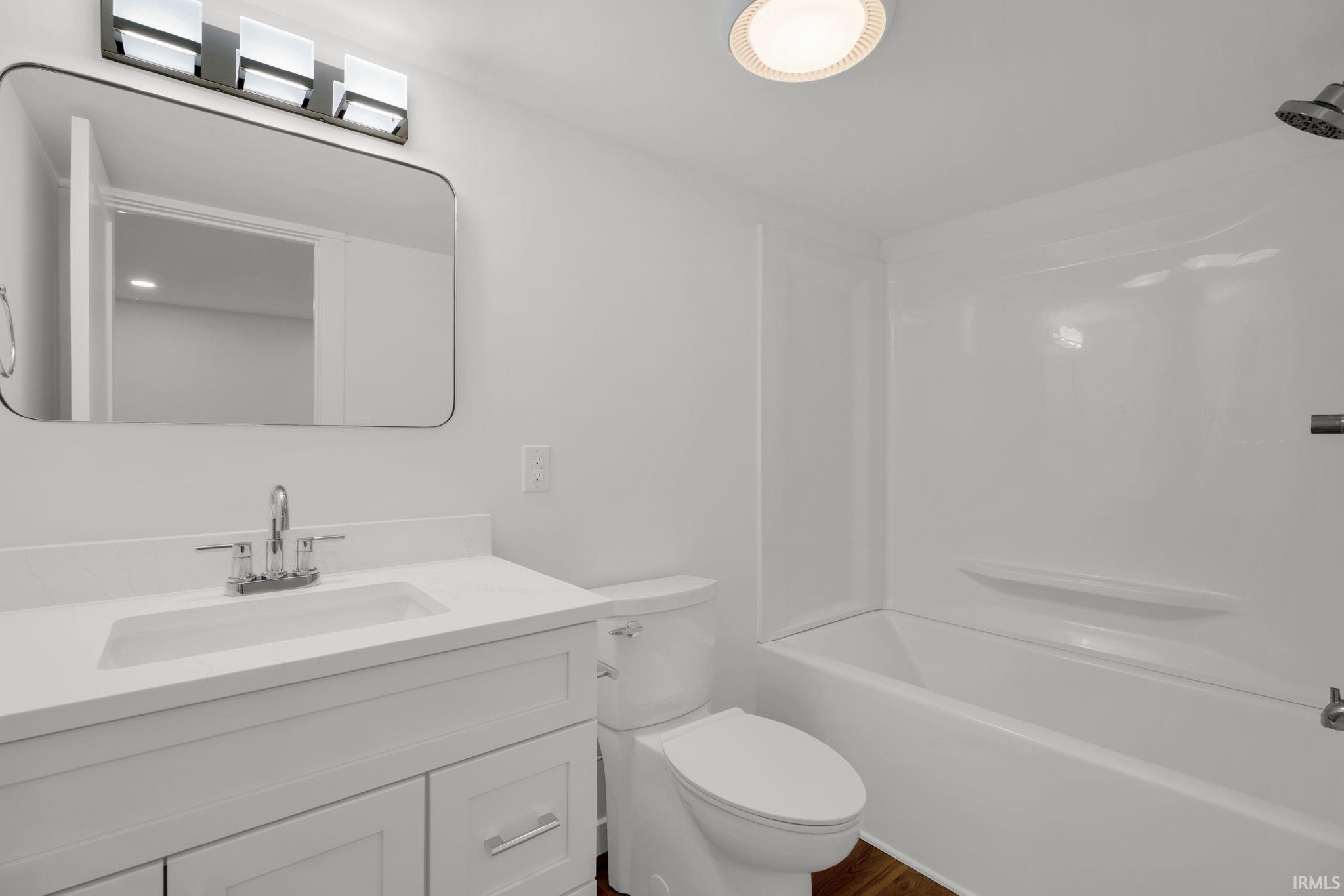 Bathroom with a white vanity, large mirror, toilet, and bathtub with a shower surround.