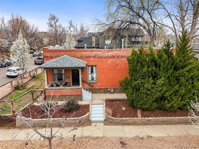 Red-brick house with a covered entry, front steps, and a large evergreen shrub.