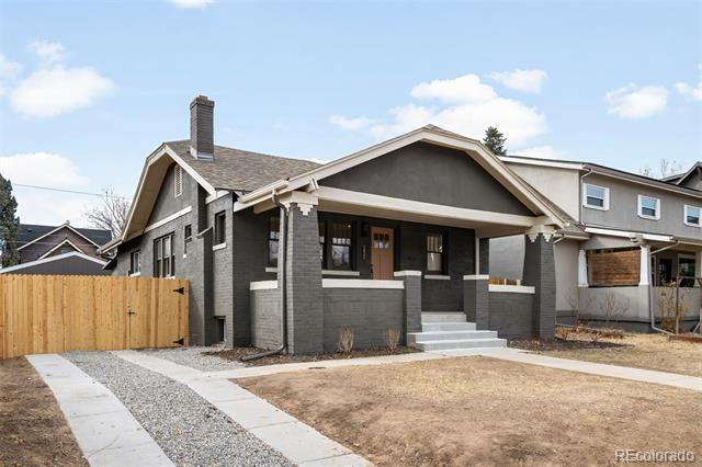 Gray brick bungalow with a covered front porch, broad steps, and a curved gravel walkway.