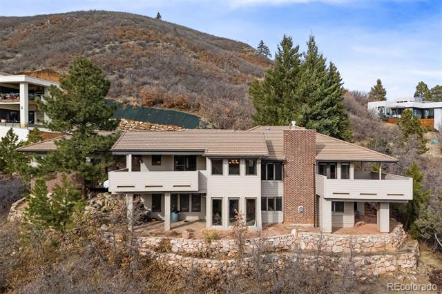 Mountain home with white balconies, a brick chimney, and stone retaining walls.