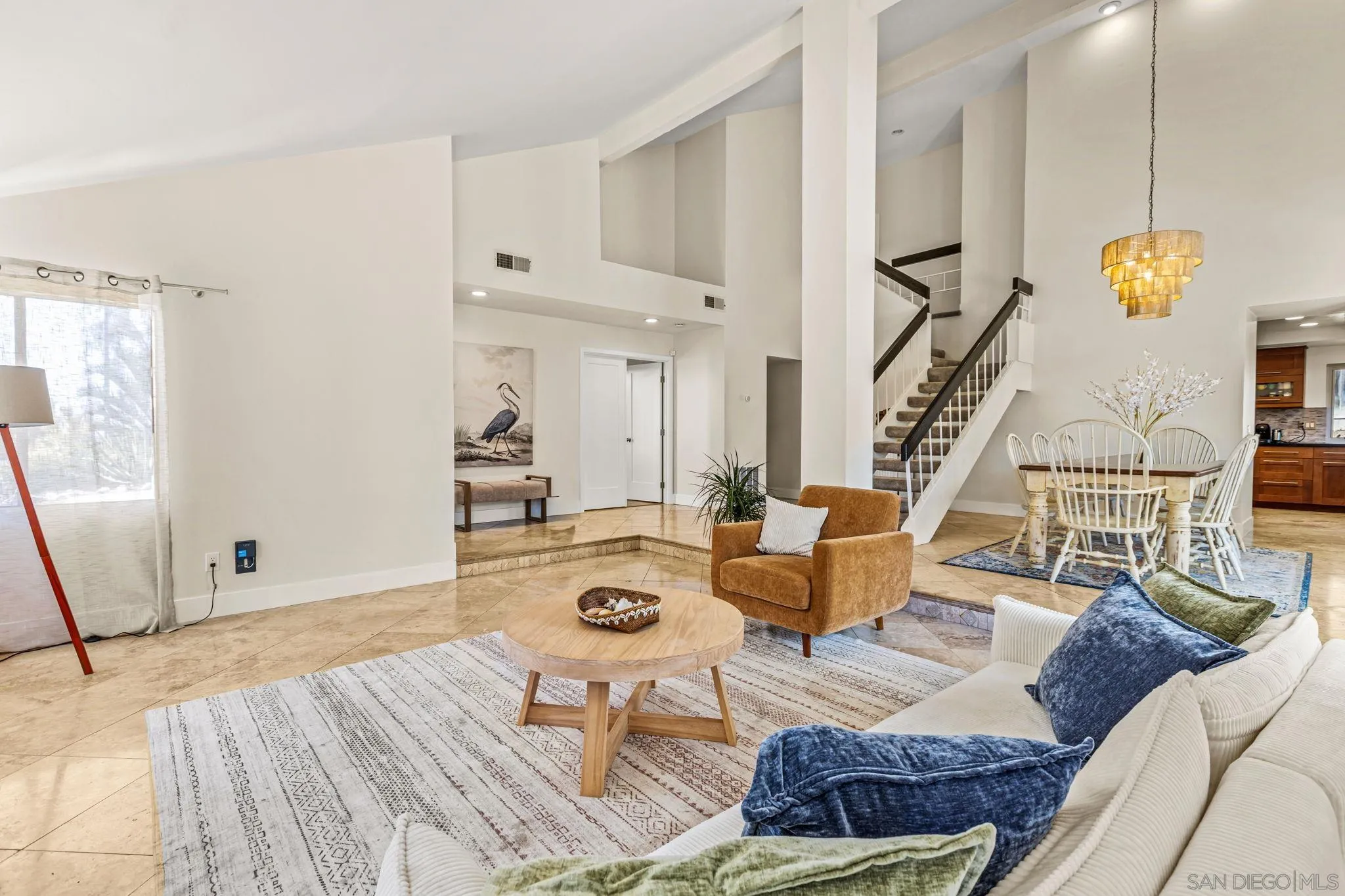 Open-plan living and dining room with high ceilings, a staircase, and a gold pendant light.