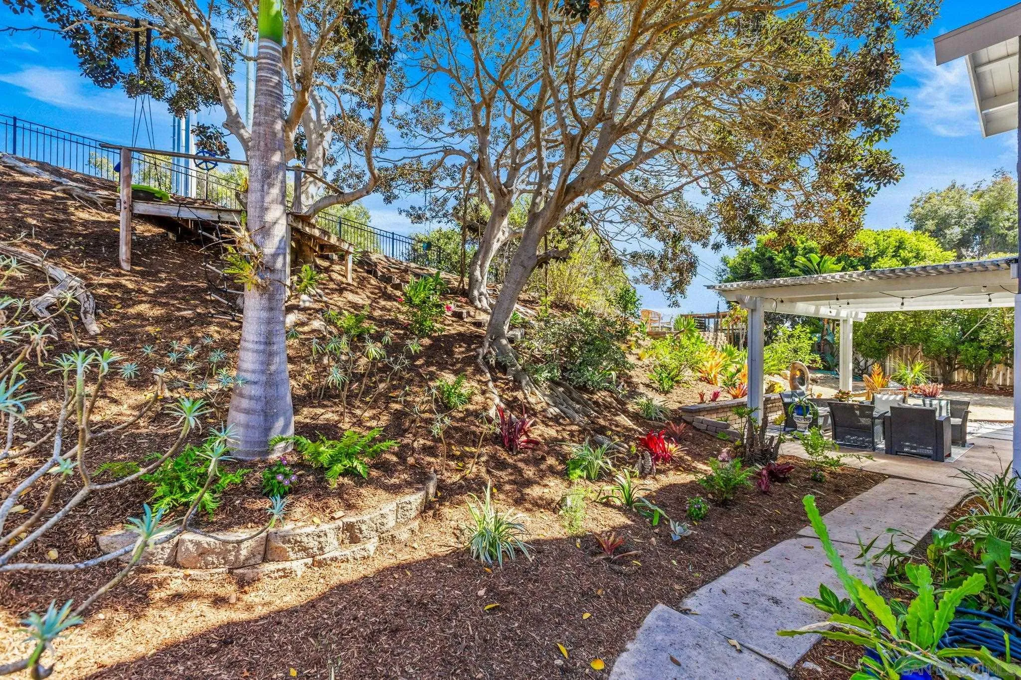 Landscaped backyard with mature trees, a planted slope, and a covered patio with outdoor seating.