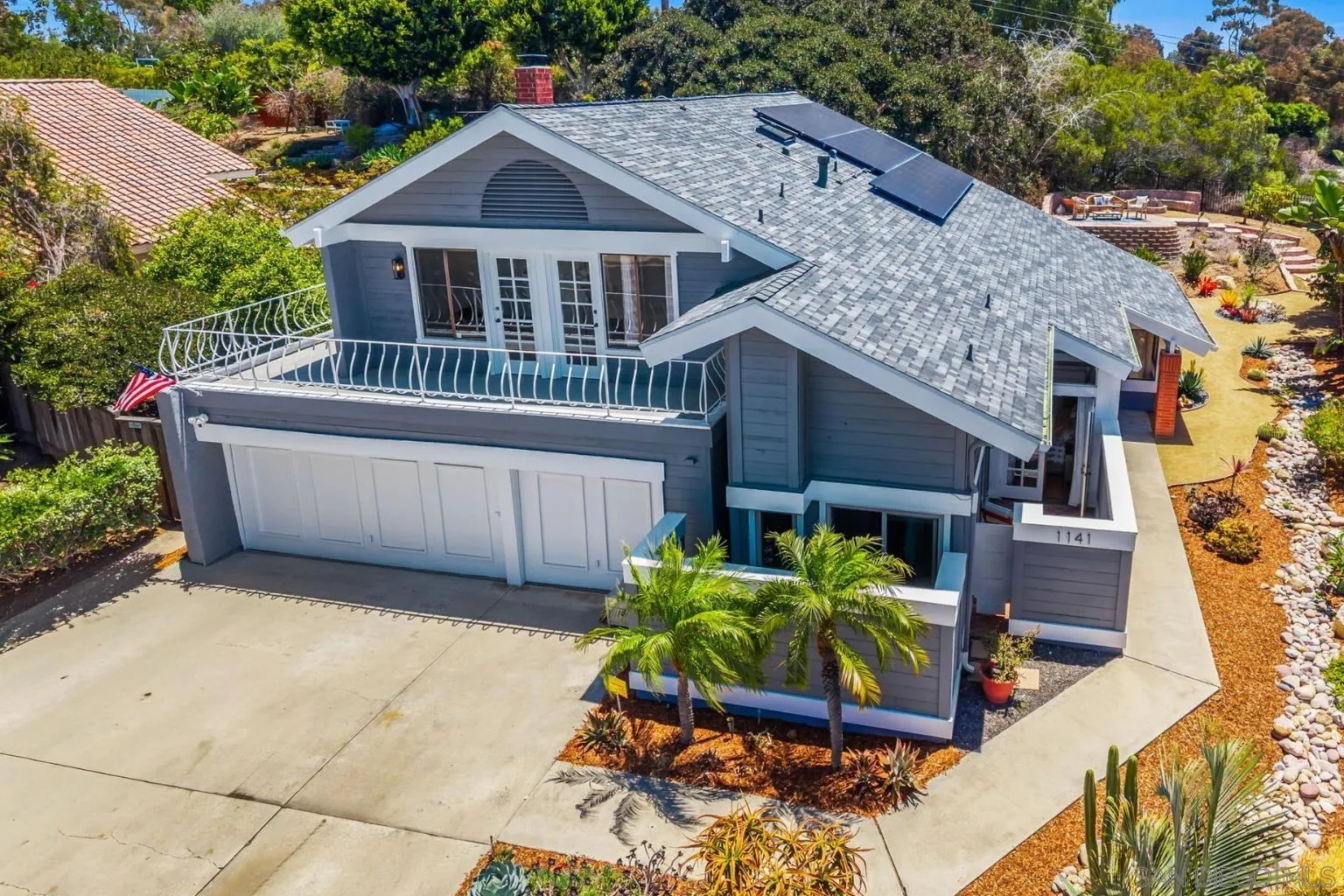 Gray two-story house with solar panels, a balcony over the garage, and landscaped grounds.