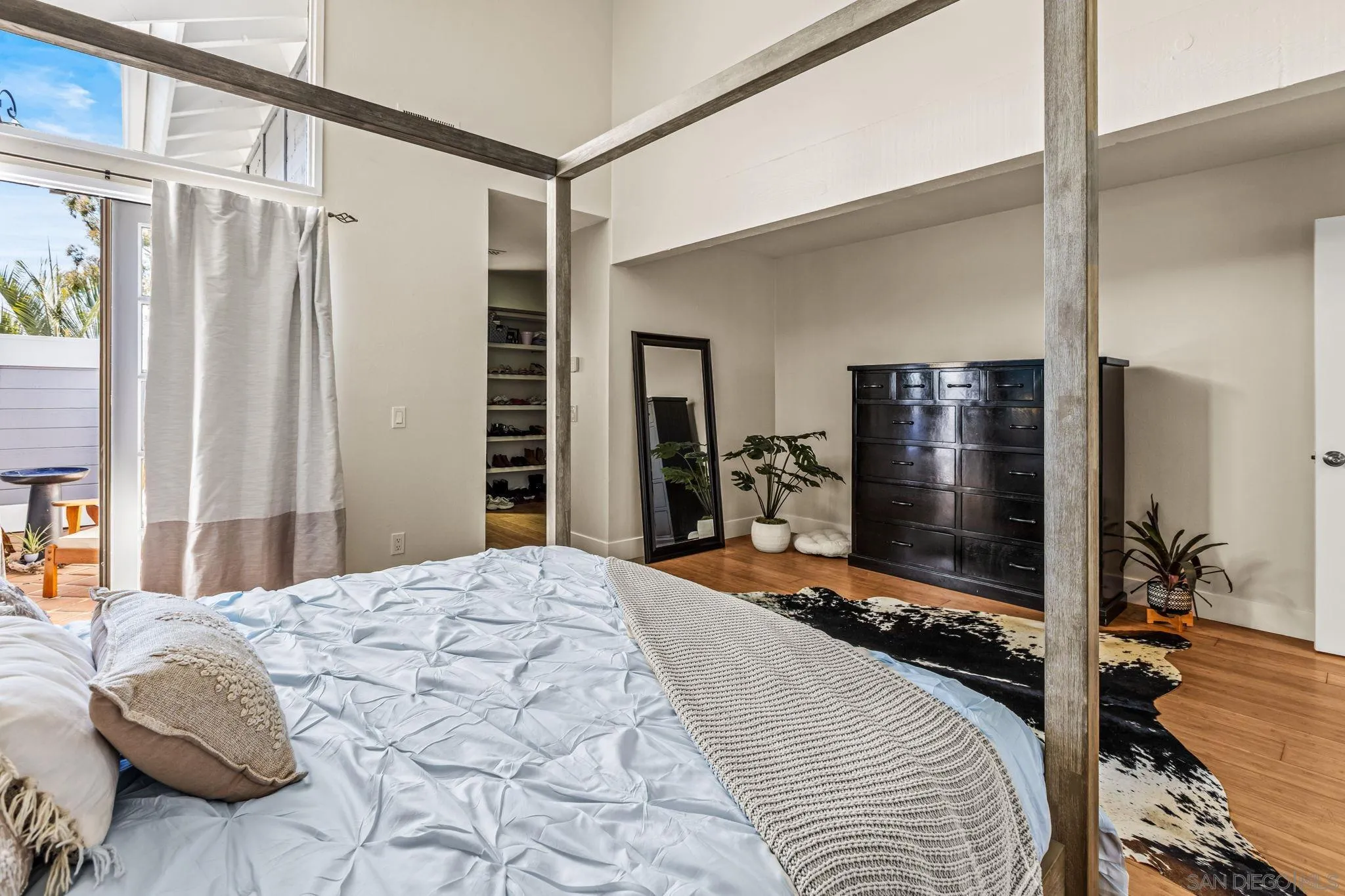 Bedroom with a four-poster bed, dark dresser, hardwood floors, and tall windows beside a patio.