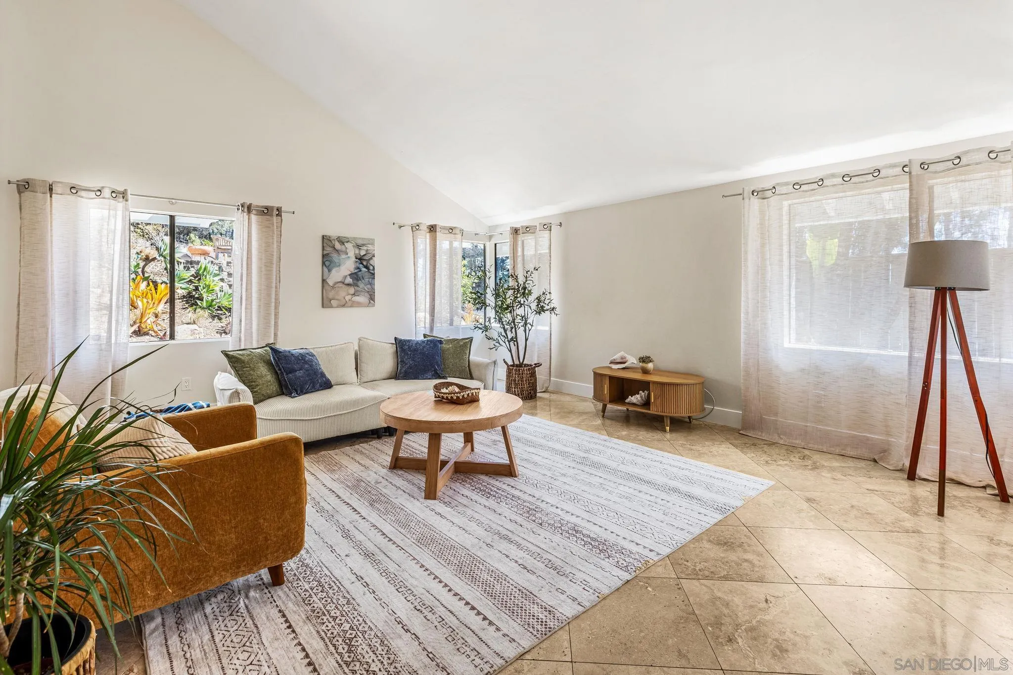 Staged living room with vaulted ceiling, large curtained windows, neutral sofa, and patterned rug.