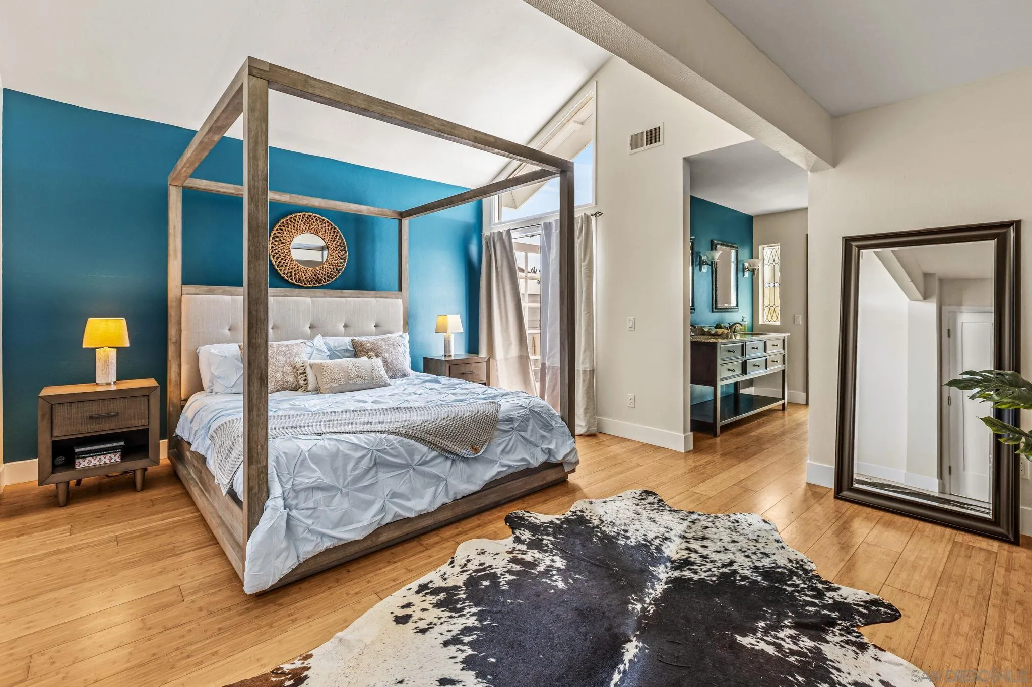Staged bedroom with a four-poster bed, teal accent wall, hardwood floors, and a black-and-white hide rug.