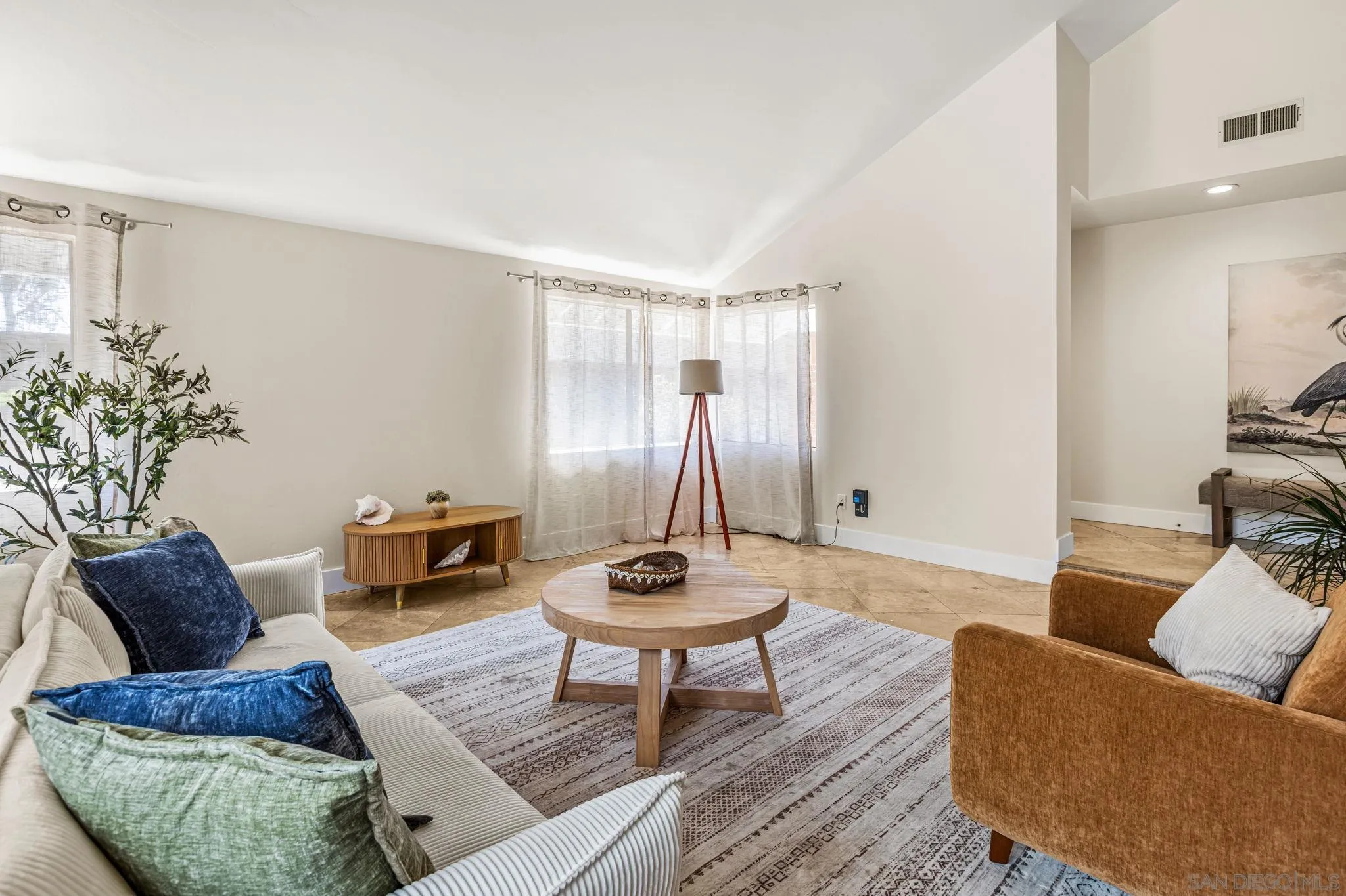 Staged living room with corner windows, a round wooden coffee table, and cream and rust-colored seating.