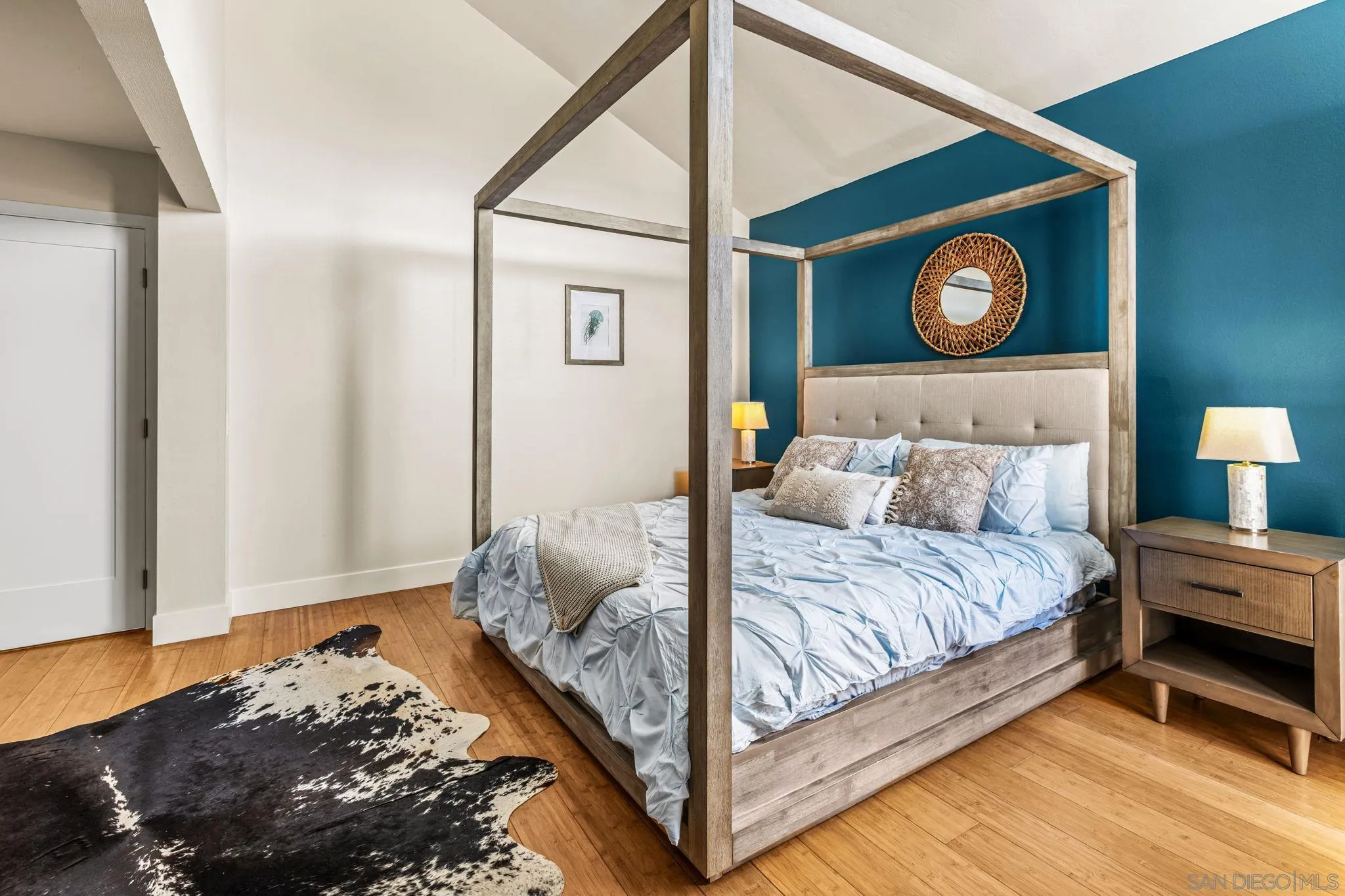 Furnished bedroom with a wooden four-poster bed, teal accent wall, and round woven mirror.