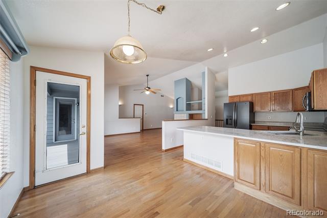 Open kitchen with a white breakfast bar, wood cabinetry, stainless steel refrigerator, and hardwood floors.