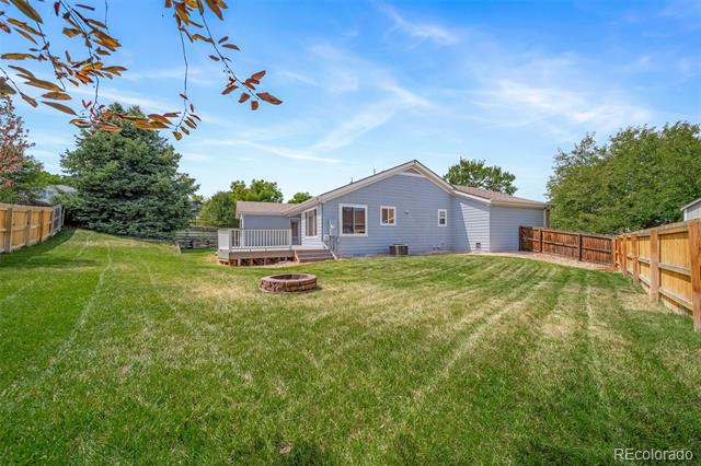 Gray single-story home behind a fenced lawn, with a small deck and circular fire pit.