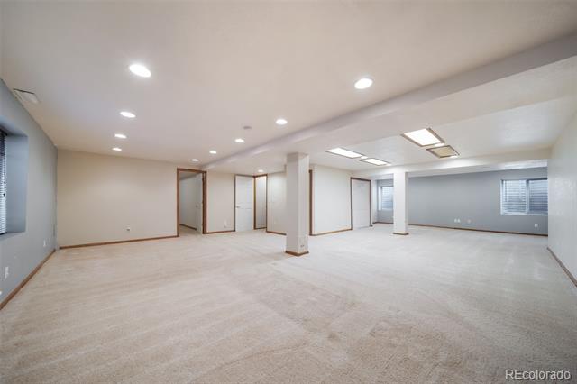 Vacant finished basement with light carpet, recessed lighting, support columns, and several windows.