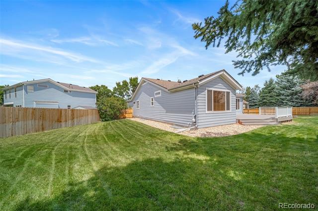 Gray-sided single-story home behind a broad green lawn, with a fenced yard and small raised deck.