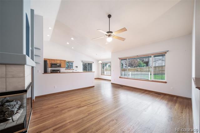 Vacant living area with wood floors, ceiling fan, large yard-facing windows, and a tiled fireplace.