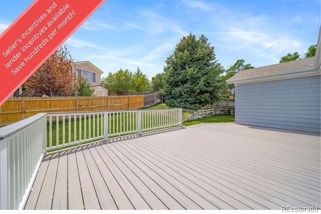 Backyard deck with white railing overlooking a fenced lawn and mature trees.