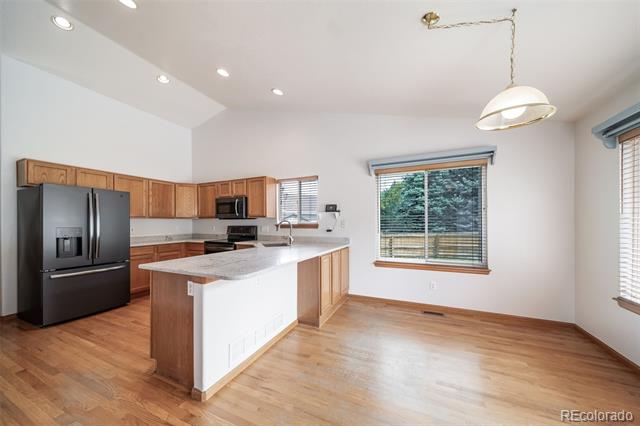 Unfurnished kitchen with wood cabinets, a large countertop peninsula, dark refrigerator, and hardwood floors.