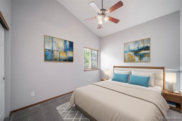 Bedroom with a cream bed, teal pillows, gray carpet, vaulted ceiling, and ceiling fan.